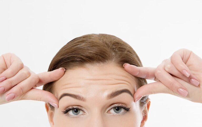 Close-up of a woman lifting her forehead with fingers, illustrating forehead wrinkles that can be treated with a BOTOX® forehead lift for smoother skin