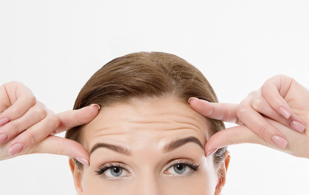 Close-up of a woman lifting her forehead with fingers, illustrating forehead wrinkles that can be treated with a BOTOX® forehead lift for smoother skin