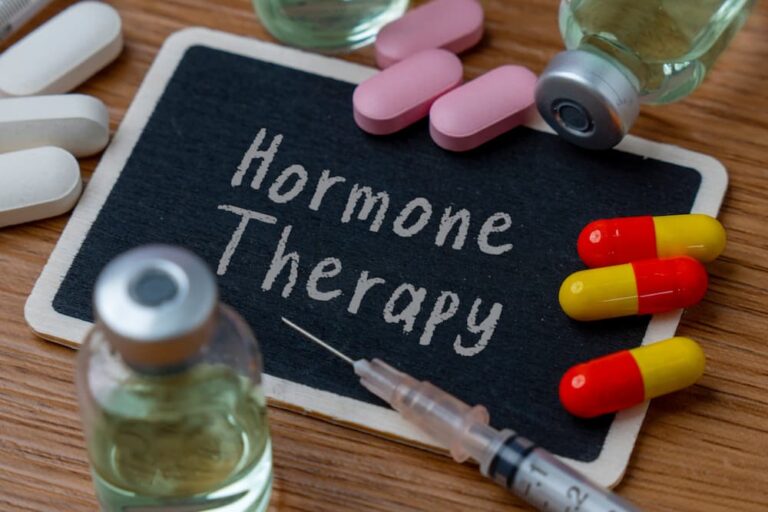 A small chalkboard labeled "Hormone Therapy" surrounded by various capsules, vials, and a syringe, representing safe hormone therapy options.