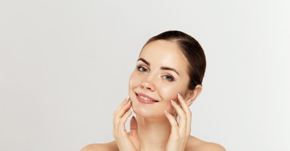 Woman with clear, smooth skin gently touching her face against a light background