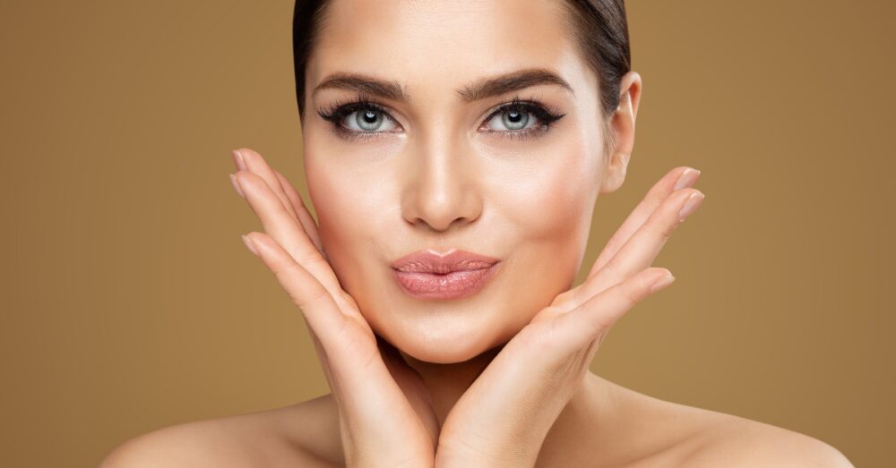 Woman with smooth skin and full lips gently framing her face with both hands
