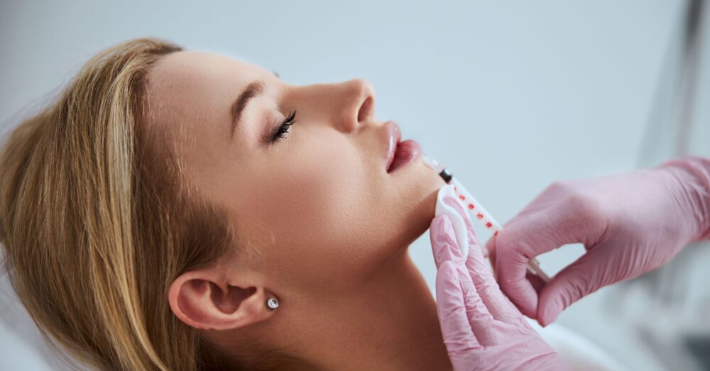 Close-up of a provider administering lip filler injections to a woman lying on a treatment table in a clinical setting