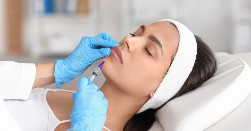 A woman in a headband receiving a facial injection from a gloved provider in a medical aesthetic clinic