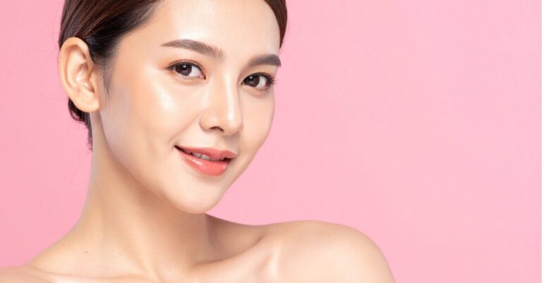 Woman with clear skin smiling softly against a pink background