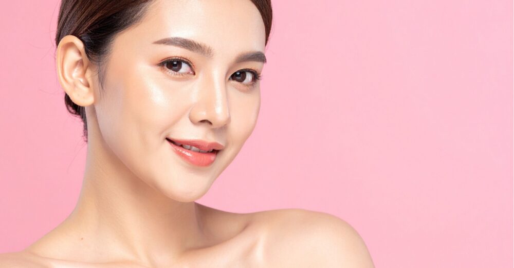 Woman with clear skin smiling softly against a pink background