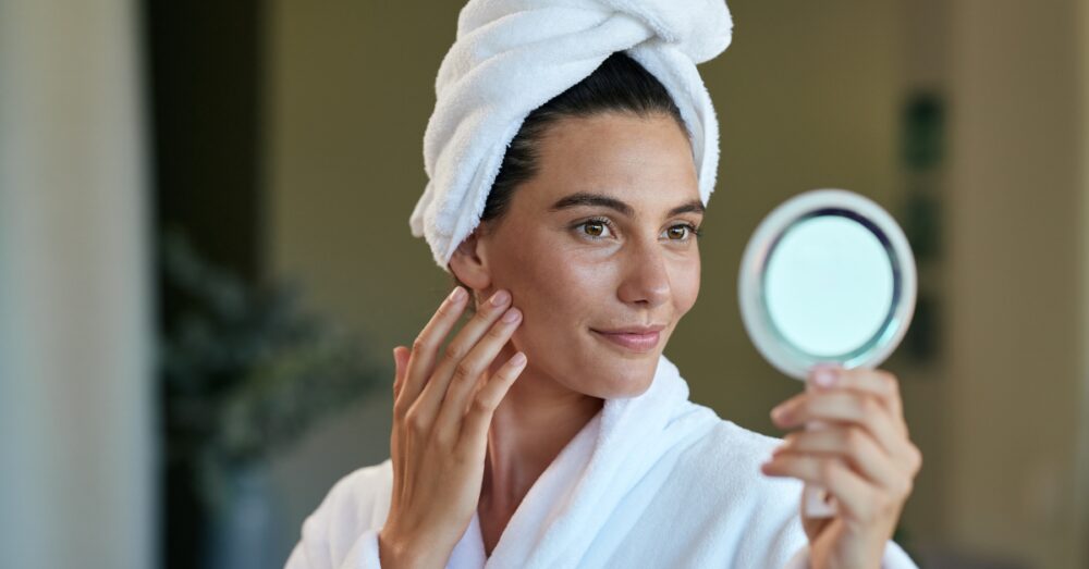 Woman in a white robe looking at her reflection in the mirror
