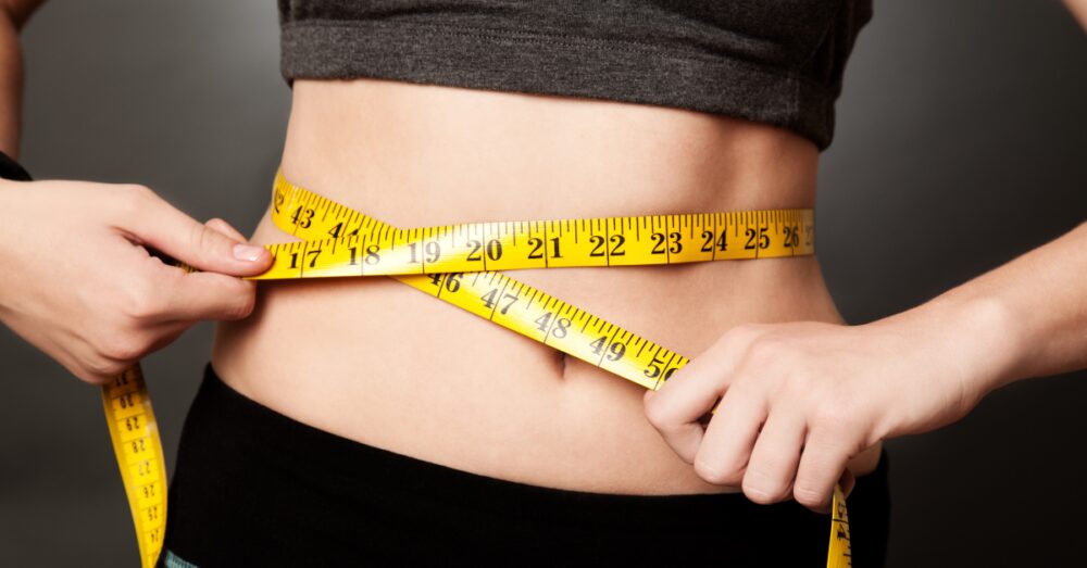 Woman with a tape measure around her waist, signifying weight loss